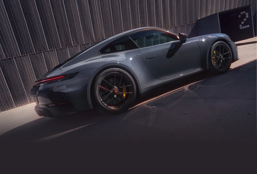 Porsche 911 Carrera GTS in Slate Grey Neo in front of a Dark Grey wall. Side view.