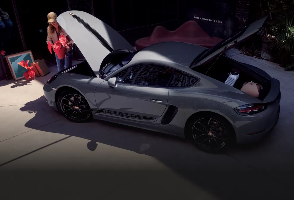Porsche 718 Cayman Style Edition en color Gris Arctic con paquete de contraste en color Negro y con maleteros abiertos mientras se está colocando carga.