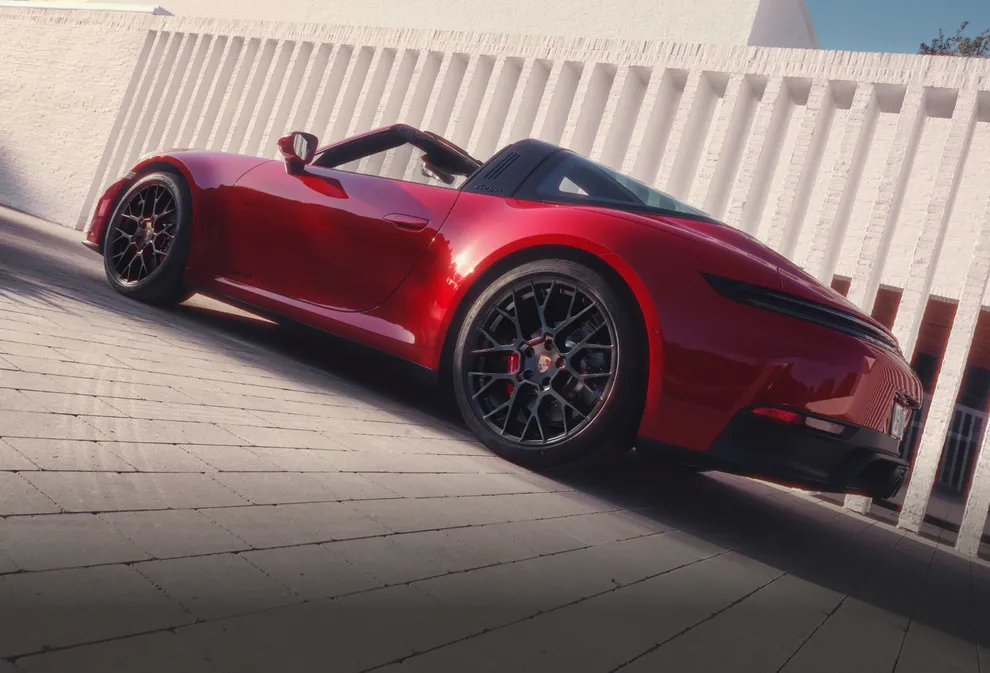 Porsche 911 Targa 4 GTS in Karminrot steht vor hellgrauer Wand. Blick auf Seite.