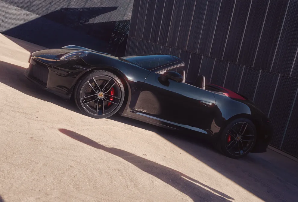 Porsche 911 Carrera GTS Cabriolet in Black in front of dark grey walls. Side view.