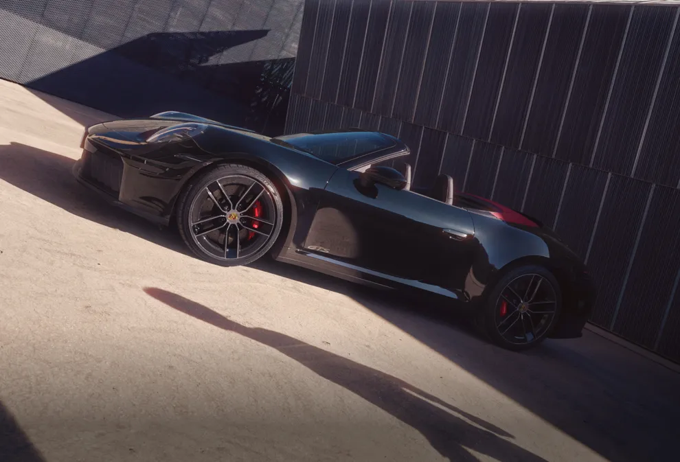 Porsche 911 Carrera GTS Cabriolet in Schwarz steht vor dunkelgrauen Wänden. Blick auf die Seite.