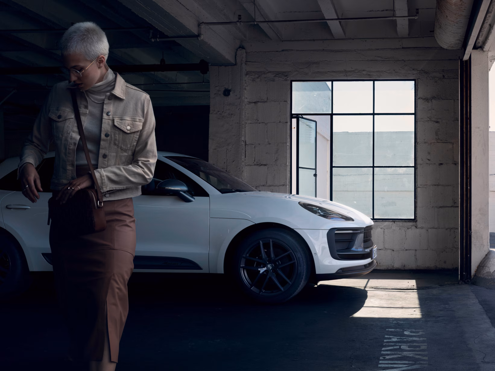 Porsche Macan T in White in a car park. View of the side. Woman walking towards the camera in the foreground.