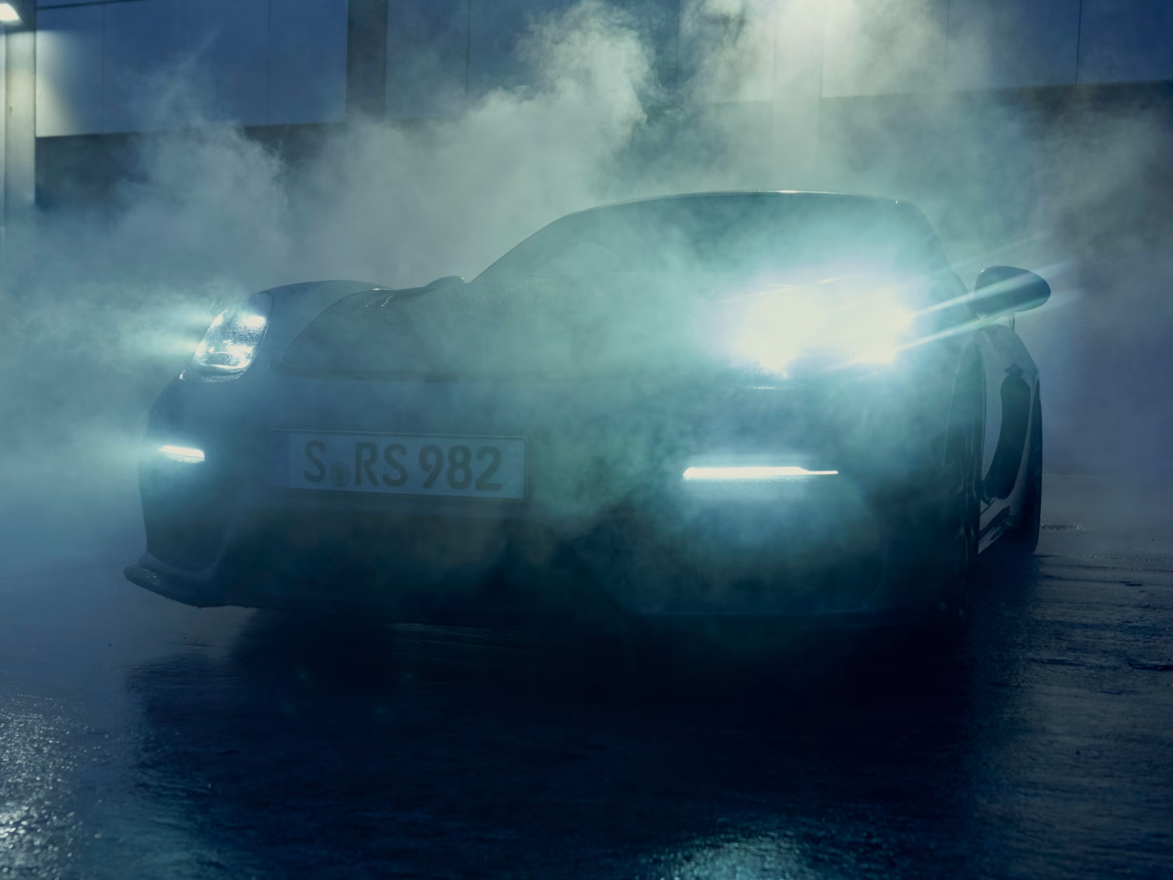 Porsche 718 Cayman GT4 RS steht mit leuchtenden Lampen im Nebel. Blick auf Front.