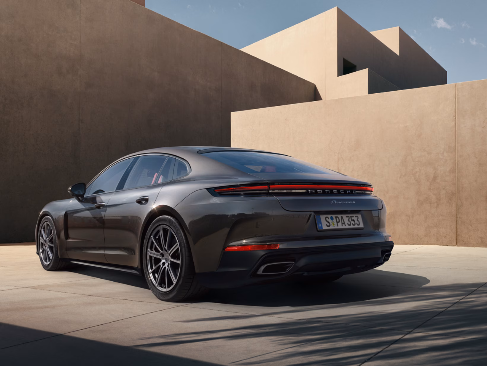 Porsche Panamera 4 in Vulcano Grey Metallic in front of concrete blocks. View of the side and rear end from behind.