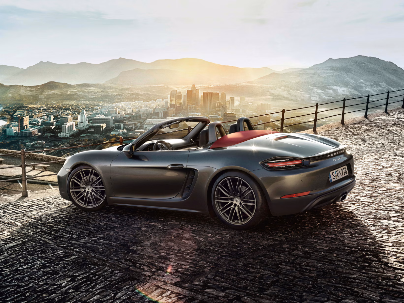 <p>Porsche 718 Boxster in Agate Grey Metallic parked at a vantage point in front of a mountain range. View of the side and rear.</p>