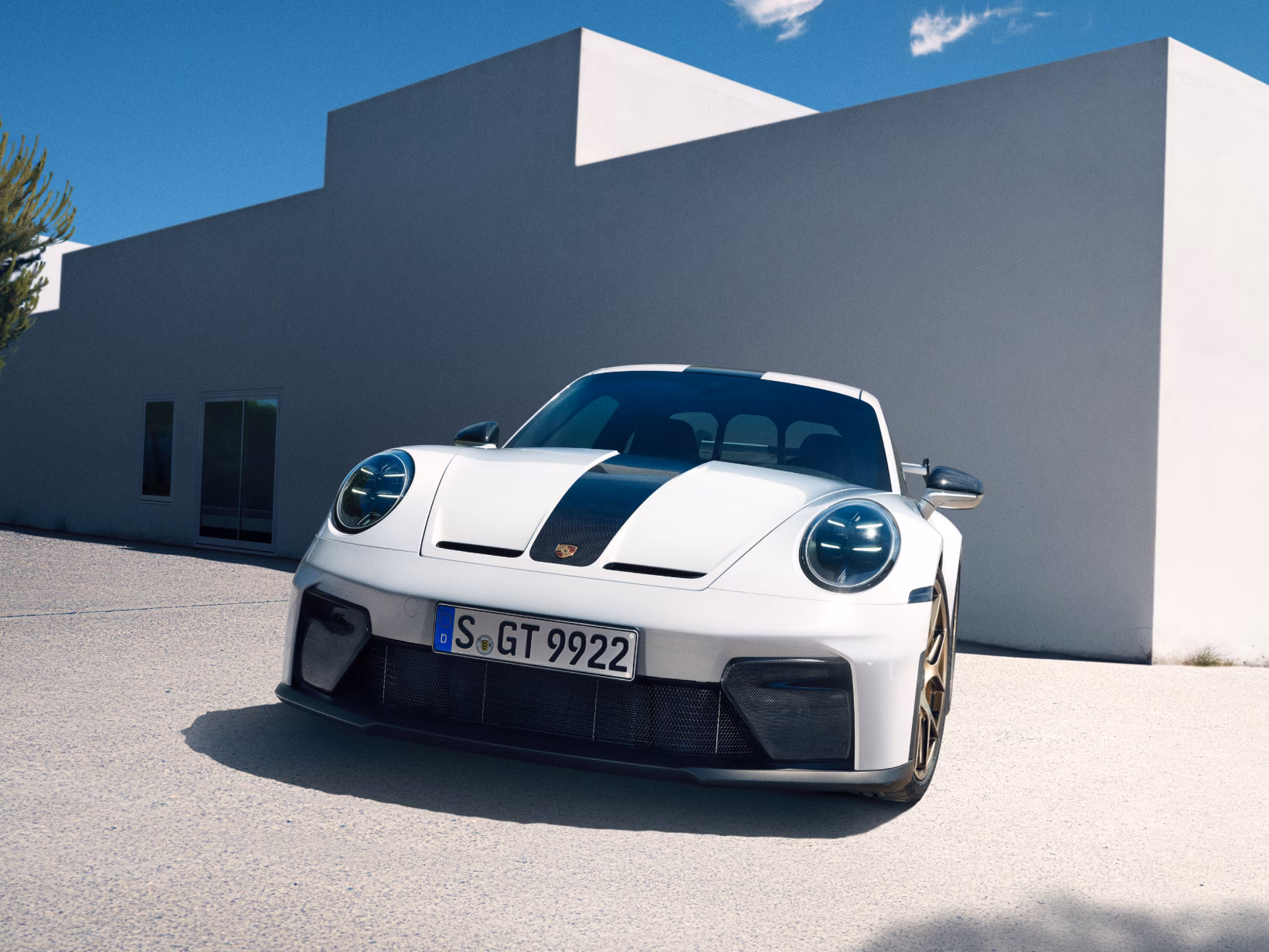 Porsche 911 GT3 in Weiß. Blick von vorne auf die Front vor einem weißen Gebäude und blauem Himmel.