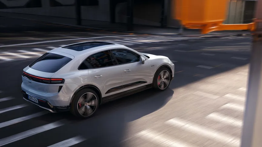 A white SUV drives through a city intersection, showcasing sleek design and tinted windows, with motion blur indicating speed.