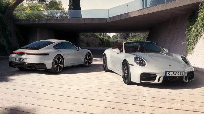 A high-angle shot shows two white Porsche 911 Carrera S, parked outside a modern house with an overhanging roof. 