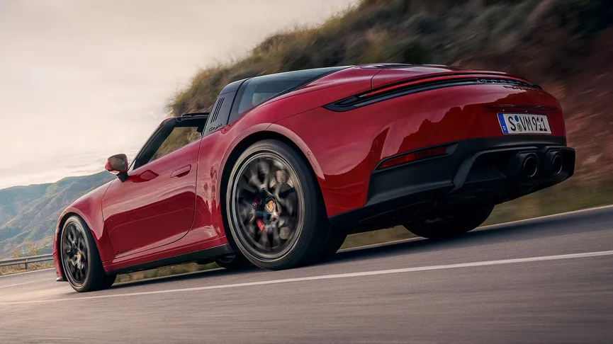 A rear-quarter-view shot of a red Porsche 911 Targa driving at speed on a winding mountain road.