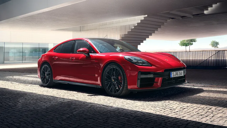A vibrant red Porsche Panamera parked under a modern, concrete structure with a staircase in the background. The car is sleek, and the setting highlights its design.