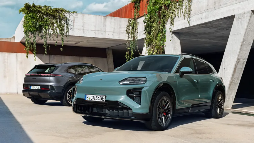 Two Porsche electric SUVs parked outside a modern concrete building with hanging greenery; a light green Porsche Cayenne Turbo Electric is in the foreground, and a dark grey Porsche Cayenne Electric is in the background.