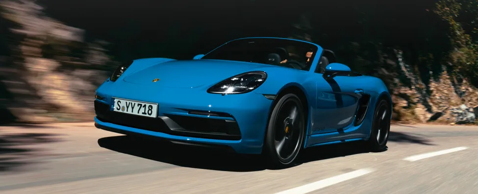 Driving shot of a Porsche 718 Boxster GTS 4.0 in Shark Blue with a view of the front and side.