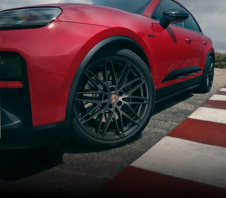 Side view of a Porsche Macan GTS Electric in Carmine Red with focus on the front wheel.