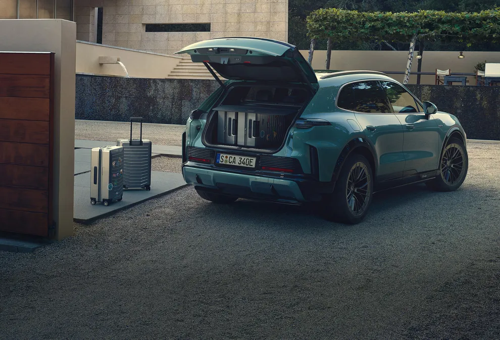 Ein Porsche Cayenne Turbo in Mysticgrünmetallic steht neben Koffern.