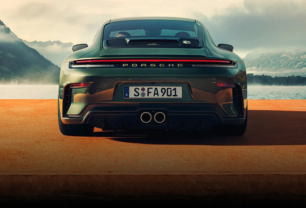 Rear view of a Porsche 911 GT3 90 F. A. in F. A. Greenmetallic on a jetty. Mountains and a lake can be seen in the background.