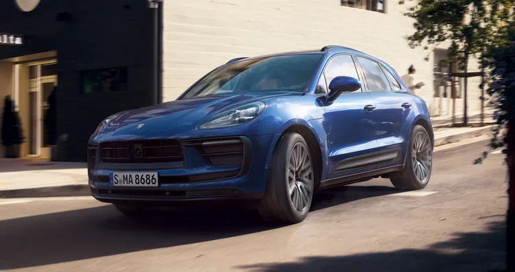 市街地を走るゲンチアンブルー メタリックのPorsche Macan。フロントビューとサイドビュー。