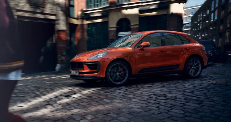 市街地の石畳の上を走り抜けるパパイヤ メタリックの Macan S。サイドビュー