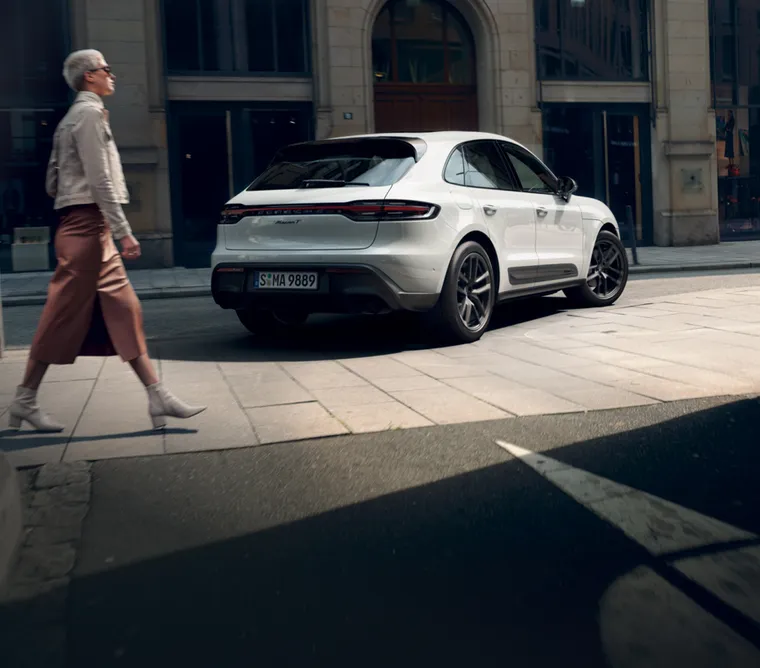 Porsche Macan T in White in a city. Rear and side view. A woman walking by.