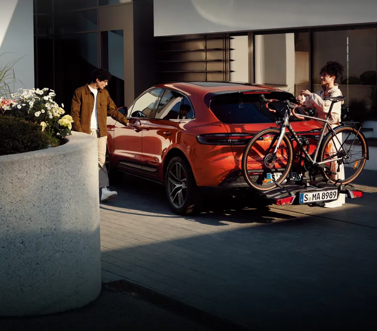 Porsche Macan S en Papaye métallisé transportant un vélo monté sur porte-vélos dans une allée. Vue de l’arrière du véhicule.