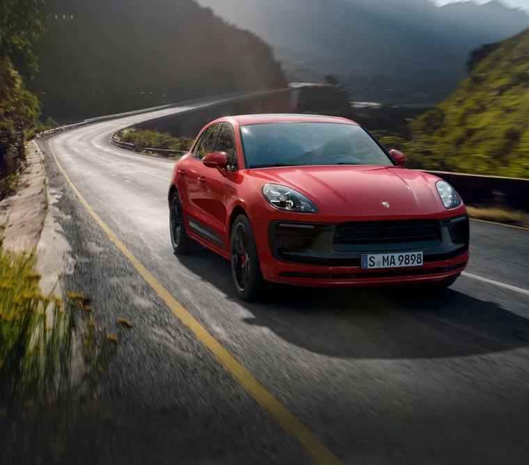Un Porsche Macan GTS en color Rojo Carmín circulando a lo largo de una carretera montañosa. Vista frontal de la parte delantera.