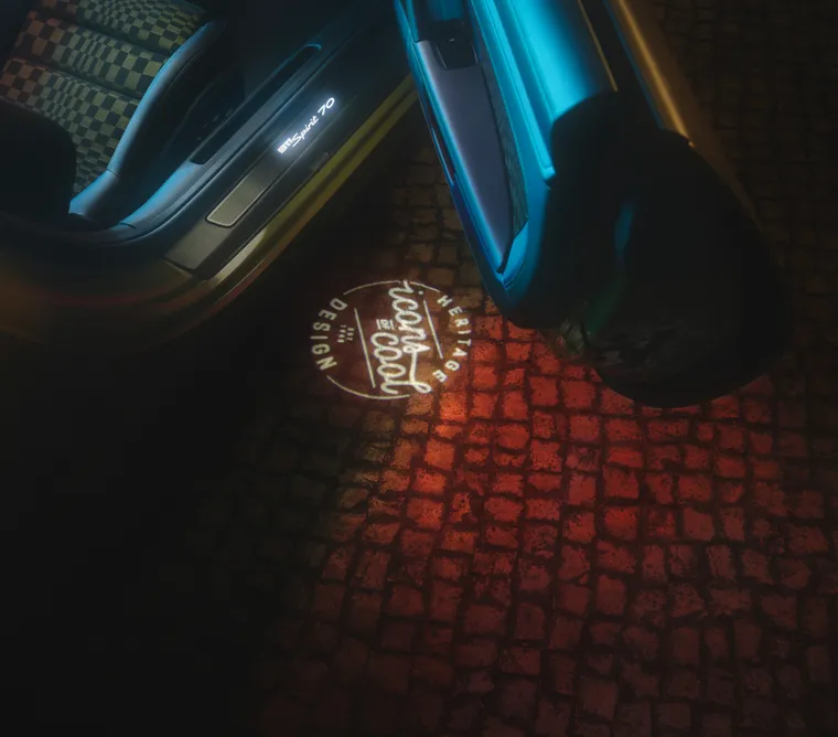 Blick von oben auf das projizierte „Icons of Cool“ Logo auf dem Boden bei geöffneter Tür des Porsche 911 Spirit 70.
