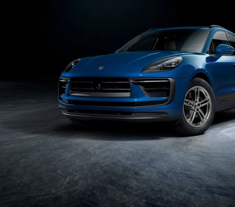 Un Porsche Macan en color Azul Gentian Metalizado frente a un fondo oscuro. Vista frontal y lateral.