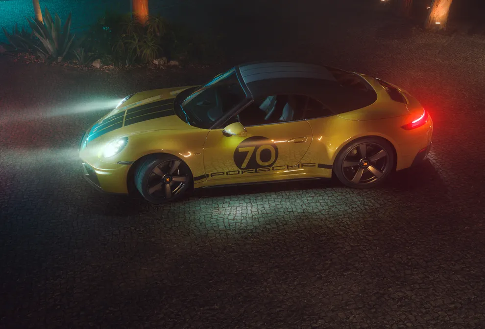 Porsche 911 Spirit 70 in an Olive Neo paint finish parked in a paved square at night with a light on. View of the side from an elevated position.