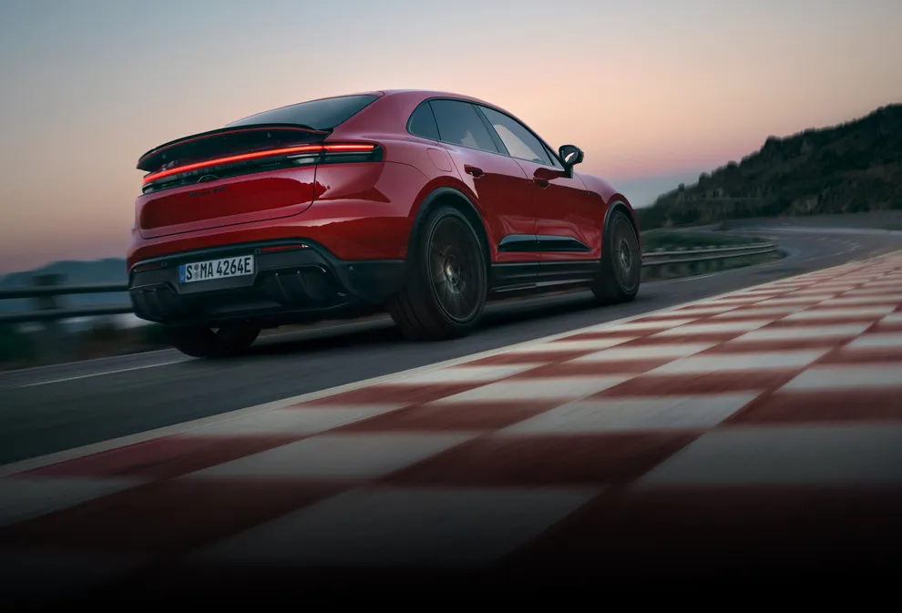 Blick von hinten auf Heck und Seite eines um die Kurve fahrenden Porsche Macan GTS in Karminrot.