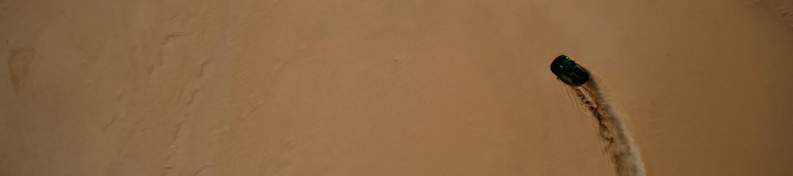 Vista dall’alto di una Porsche Macan 4S che guida sulla sabbia del deserto.