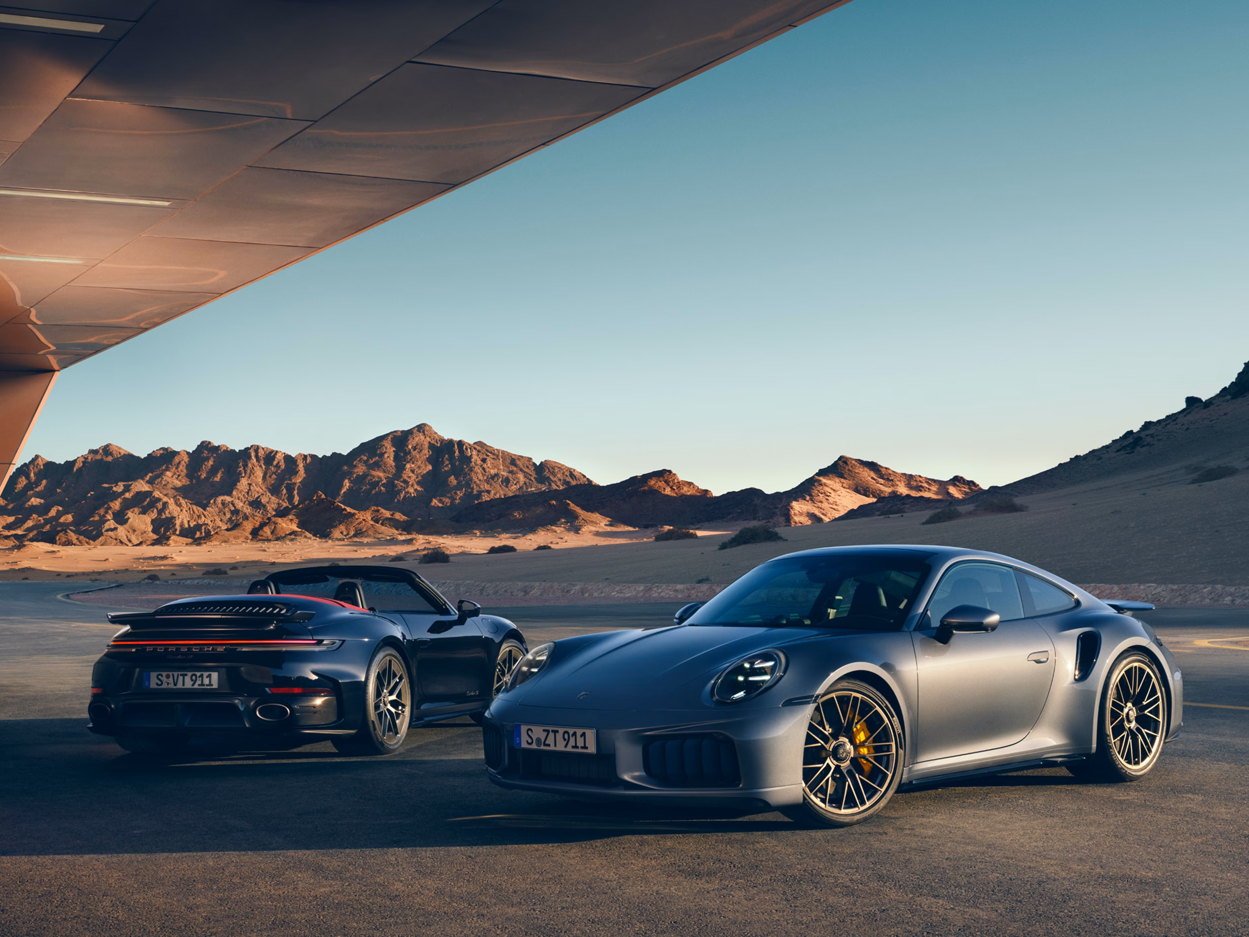 Ein Porsche 911 Turbo S in Vanadiumgraumetallic und ein Porsche 911 Turbo S Cabriolet in Tiefschwarzmetallic stehen nebeneinander.