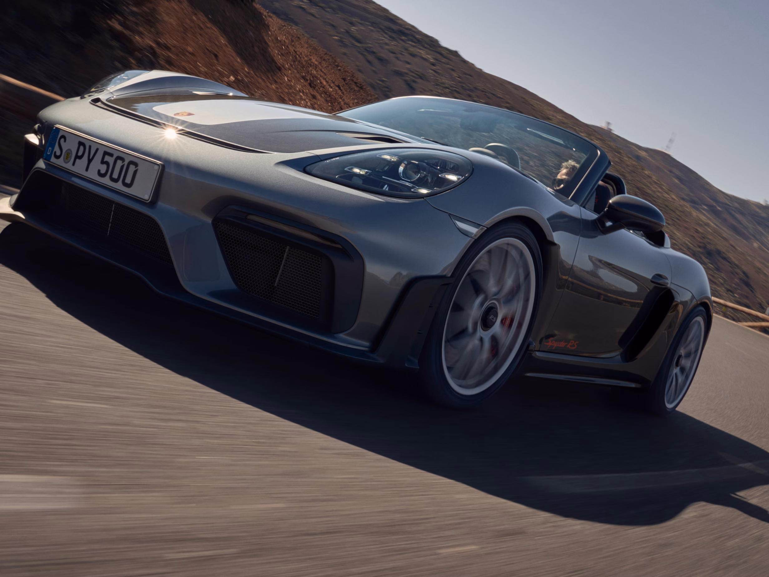 Porsche 718 Spyder RS in Vanadiumgraumetallic fährt über Straße. Sicht  auf  das Heck mit Heckspoiler, Diffusor und Endrohren.