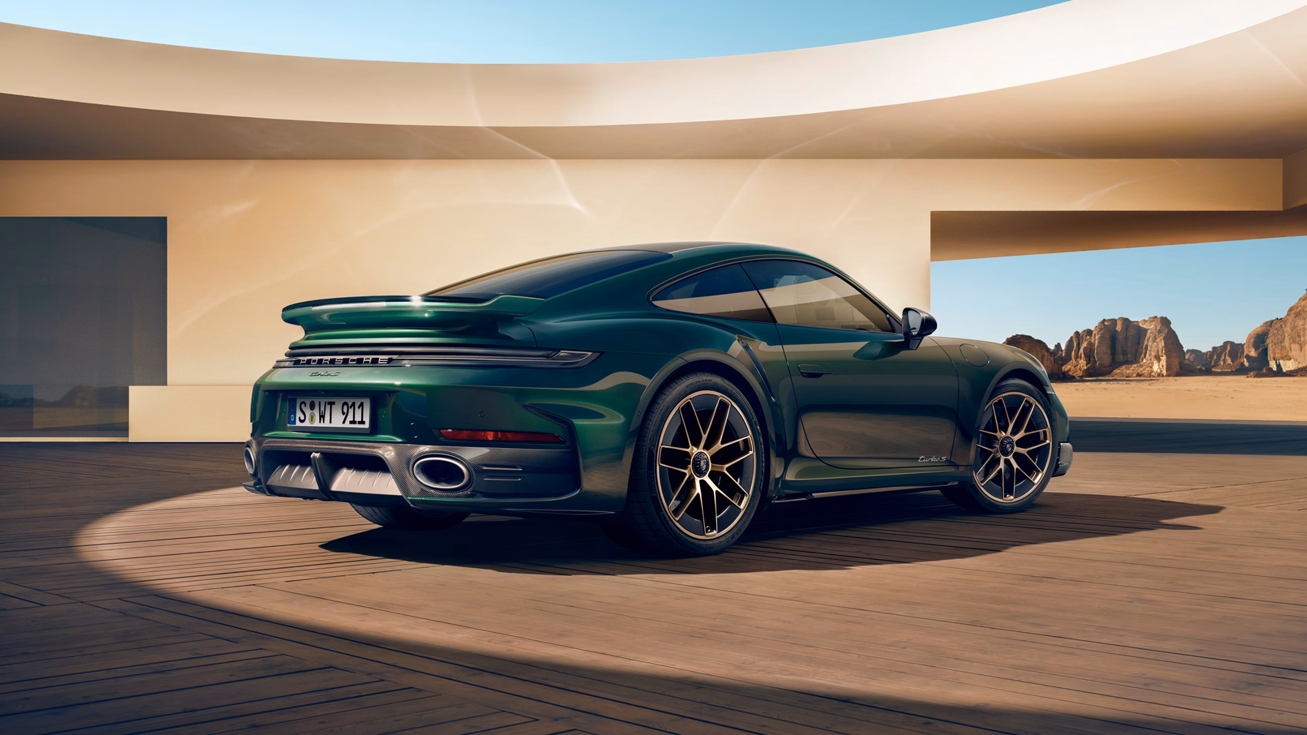 View of the rear and side of a Porsche 911 Turbo S in Oak Green Metallic Neo, standing in a courtyard.