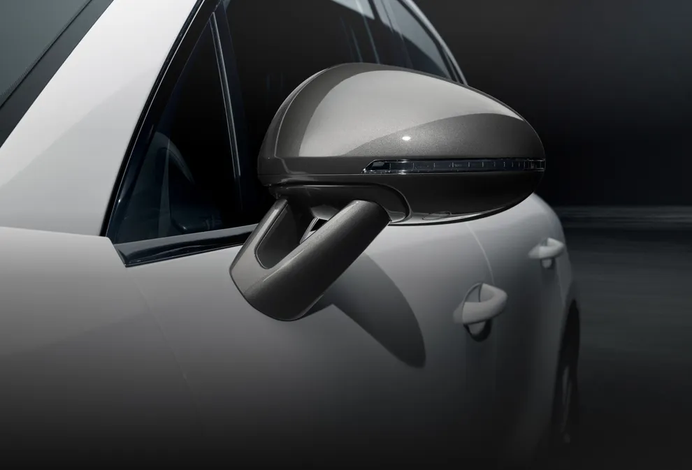 Detailed view of the exterior mirror of a Porsche Macan T in White against a dark background.
