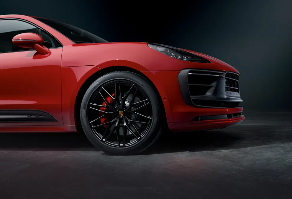 Un Porsche Macan GTS en color Rojo Carmín frente a un fondo oscuro. Vista lateral de la parte delantera.