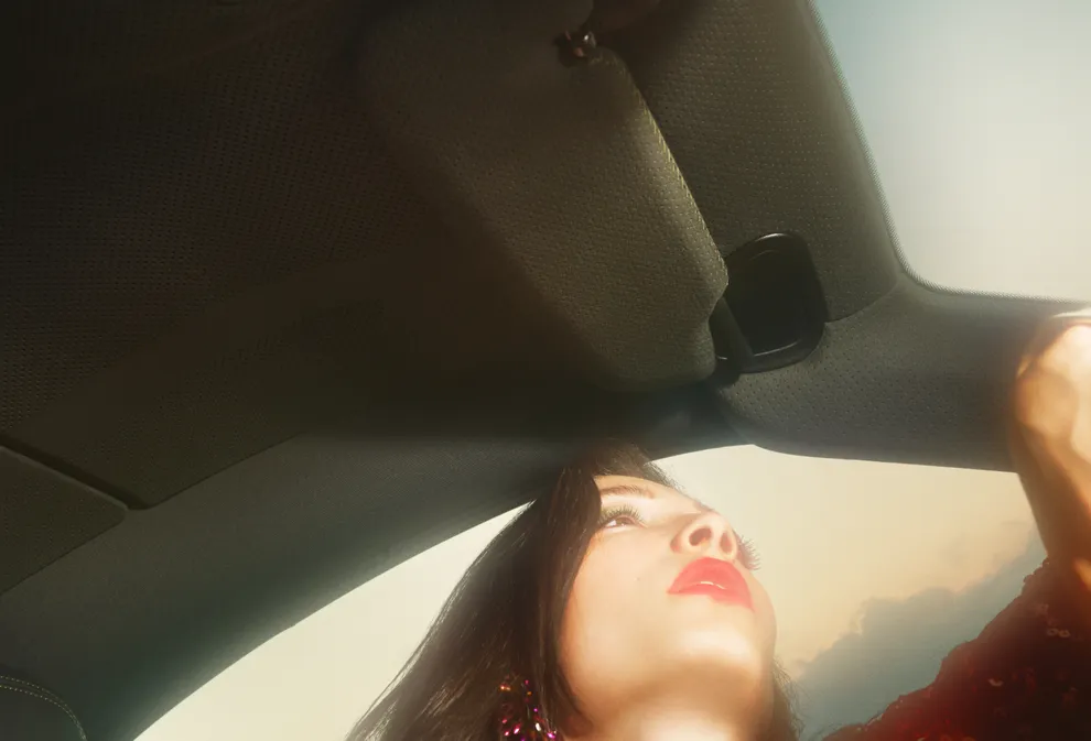 Blick von unten auf das Gesicht einer Frau mit rotem Lippenstift und den Dachhimmel des Porsche 911 Spirit 70 aus Race-Tex.