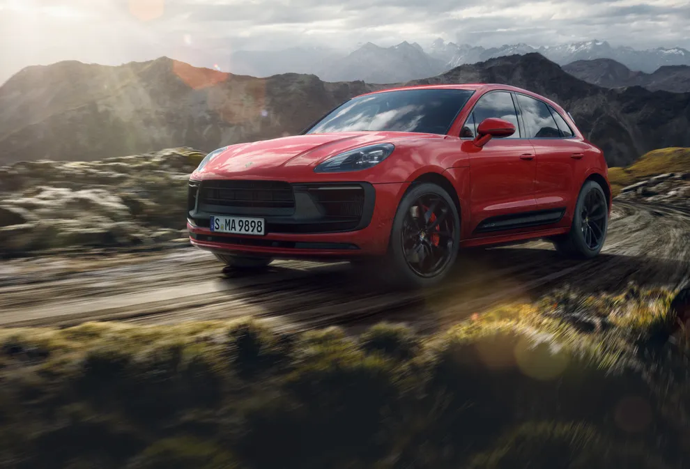 Porsche Macan GTS in Carmine Red driving through a mountain landscape. Front and side views.