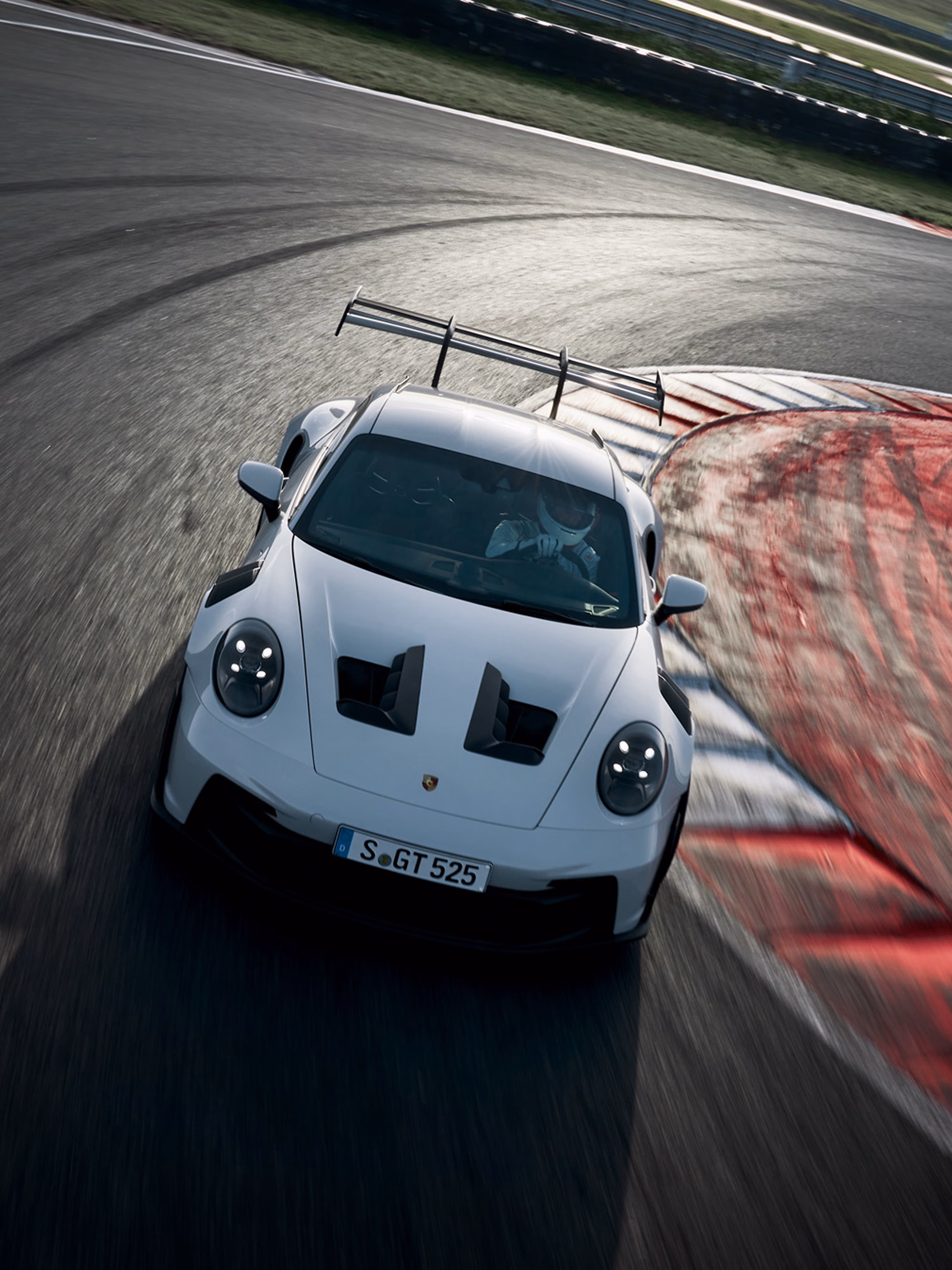 The Porsche 911 GT3 RS in Ice Grey Metallic on a race track. Front view of the front. A racing driver is standing the foreground.