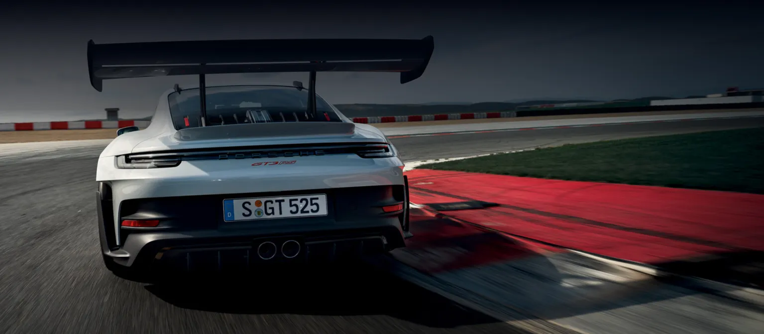 Porsche 911 GT3 RS in Eisgraumetallic fährt auf Rundstrecke um Kurve. Blick von hinten aufs Heck.