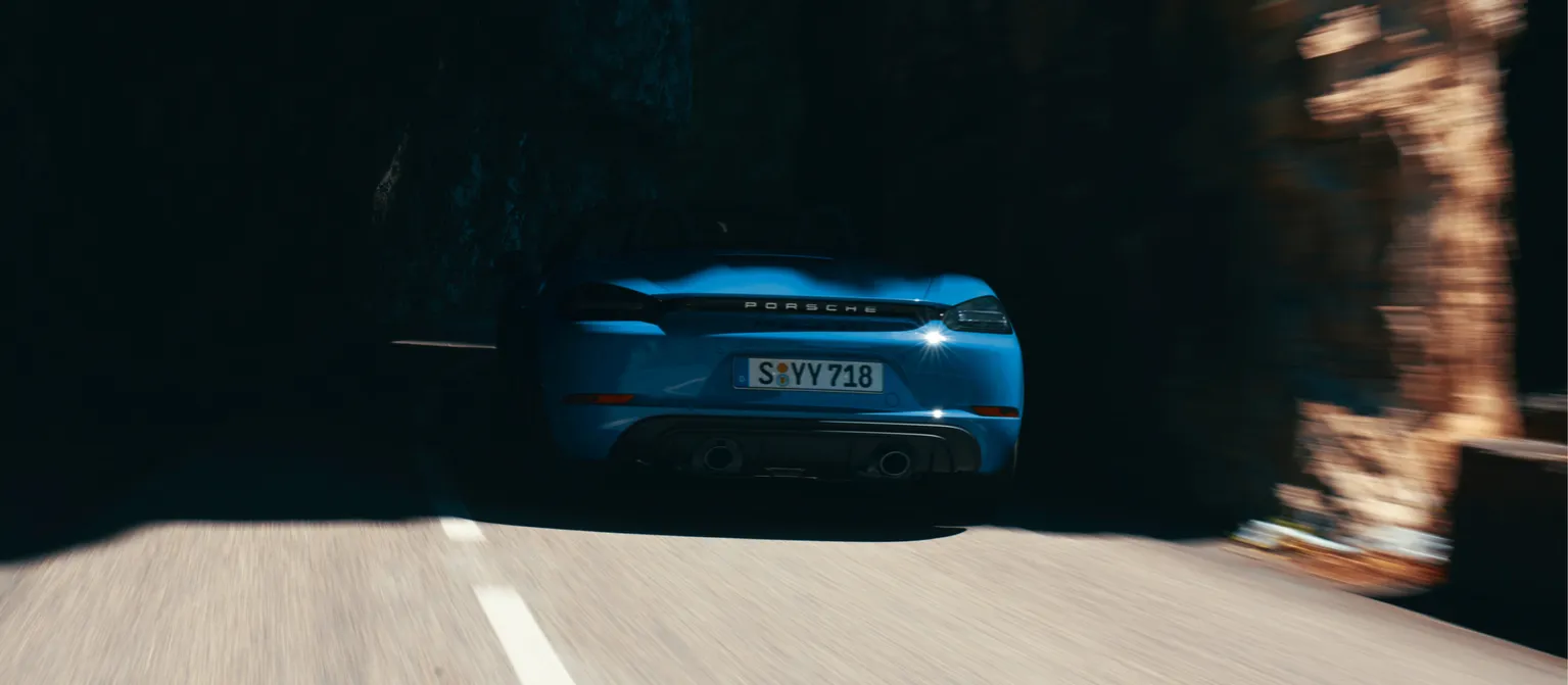 Fahraufnahme eines Porsche 718 Boxster GTS 4.0 in Sharkblue. Blick aufs Heck. Fahrzeug verschwindet in dunklem Tunnel.