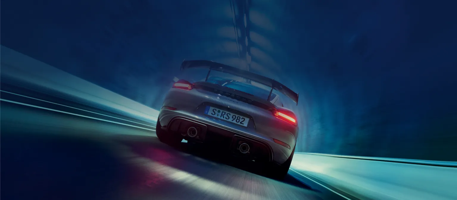 Porsche 718 Cayman GT4 RS in grigio artico con pacchetto Weissach passa in un tunnel. Vista del posteriore con dettaglio dei terminali di scarico.