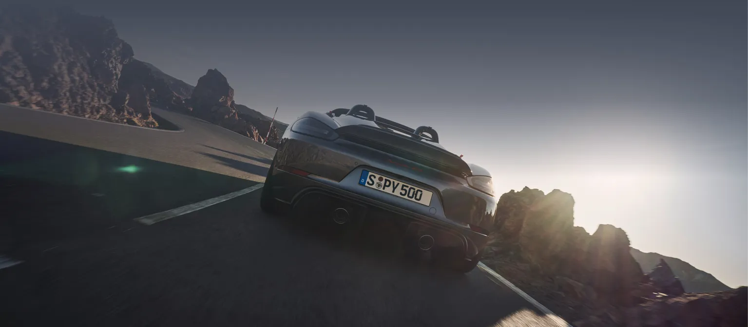 <p>Porsche 718 Spyder RS na cor Cinzento Vanádio Metálico e sem capota desloca-se na estrada. Vista de baixo, de trás, da traseira.</p>