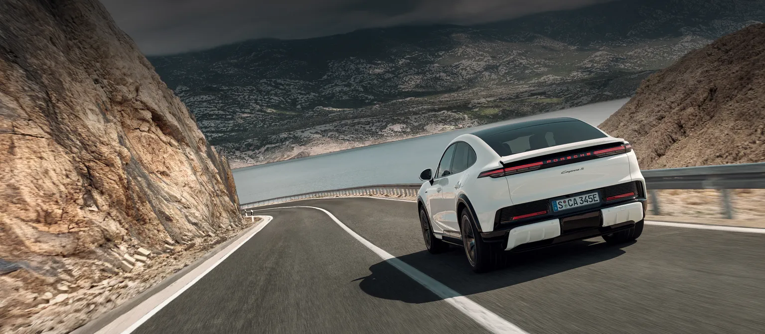 A Porsche Cayenne Turbo Coupé driving on a country road. View of the rear.