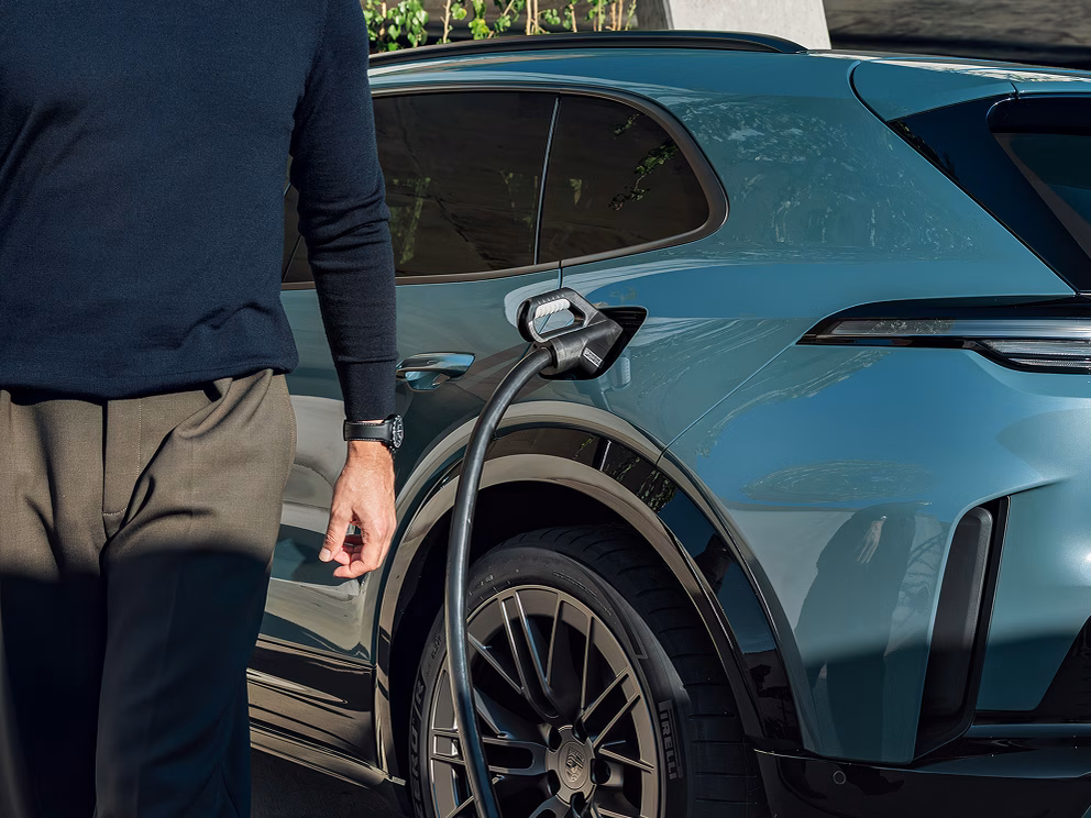 A Porsche Cayenne Turbo in Mystic Green Metallic charging at a charging pedestal.