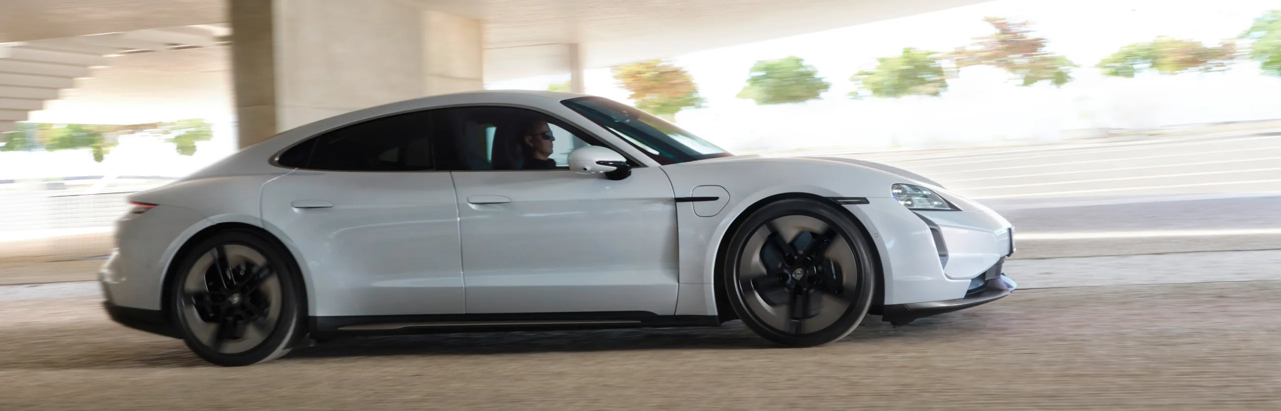 Porsche Taycan Turbo S in Ice Grey Metallic driving along a city street. Side view.