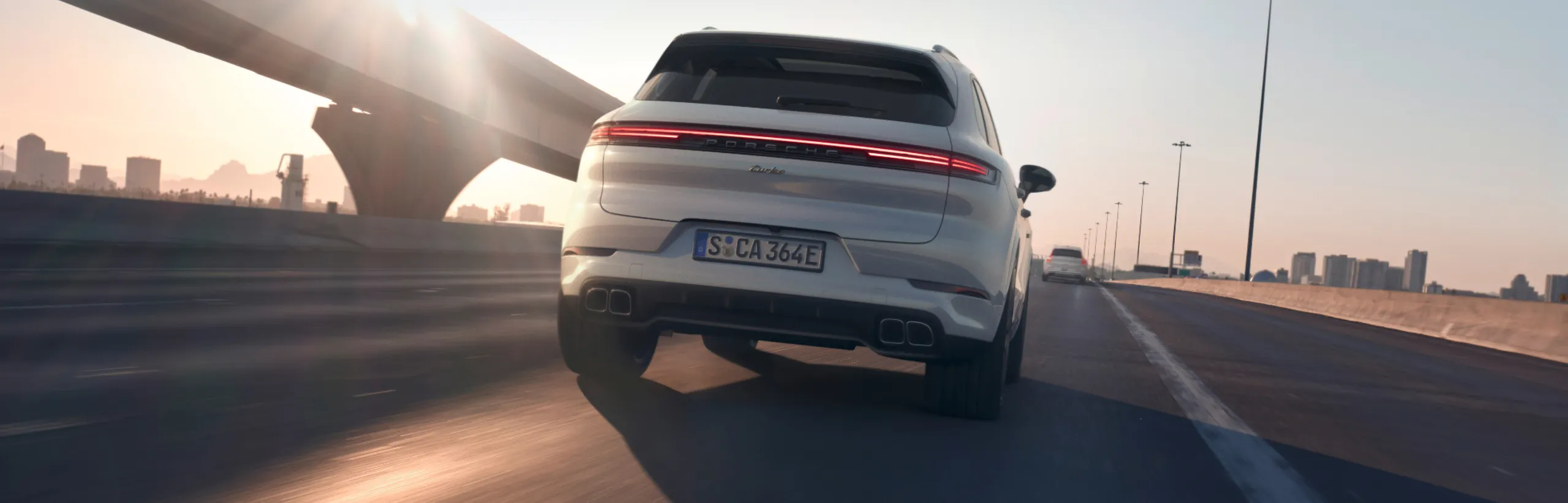 Porsche Cayenne Turbo E-Hybrid in Carrarawit metallic rijdt op de snelweg. Blik van achteren op de achterkant.