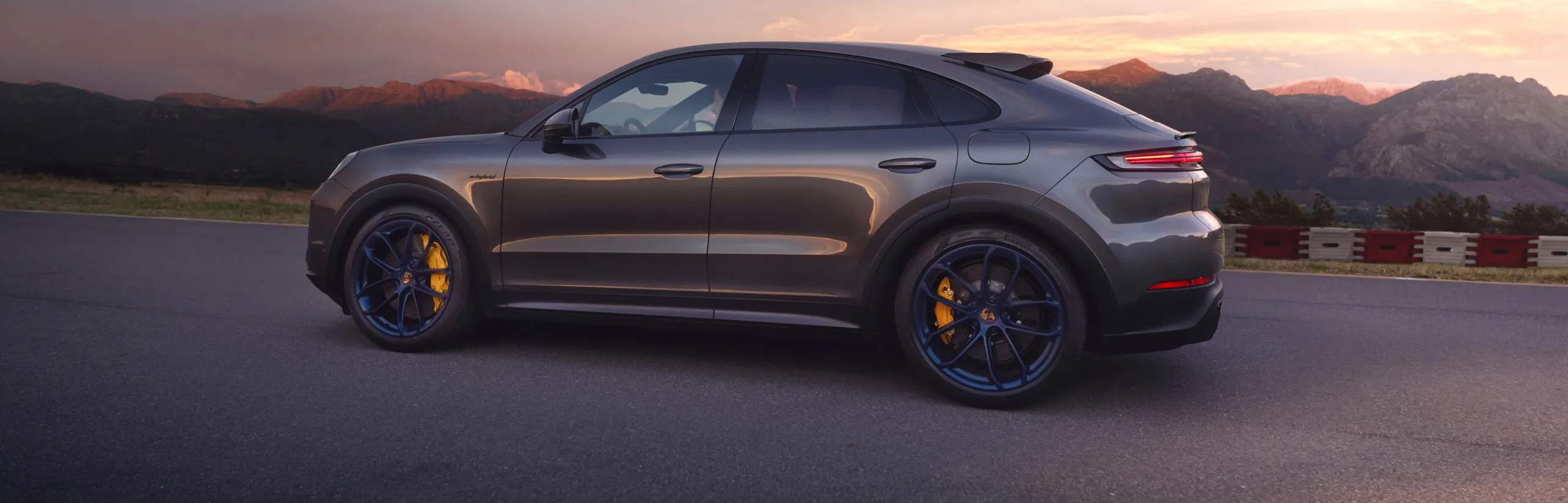 Porsche Cayenne Turbo E-Hybrid Coupé with GT package in Quarzite Grey Metallic parked in front of a scenic landscape. Side view.
