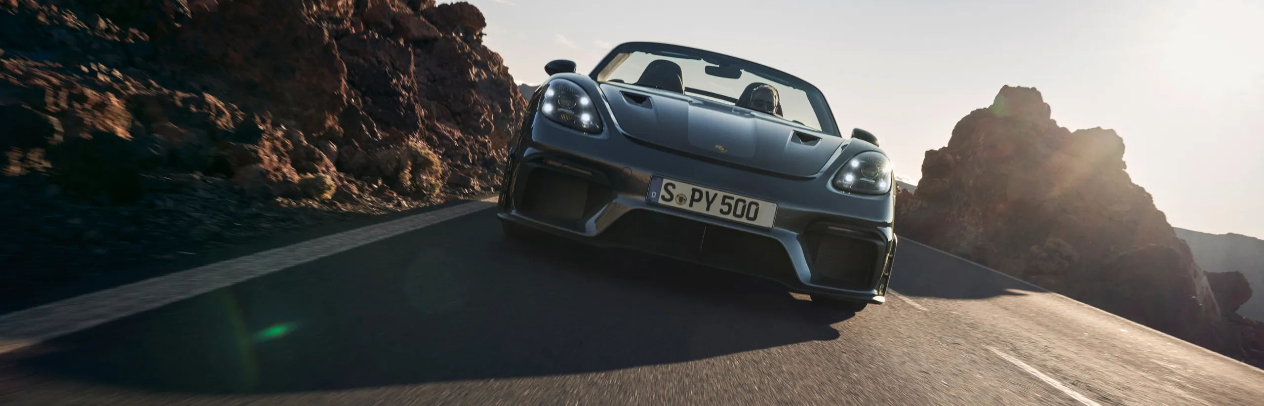 Porsche 718 Spyder RS in Vanadium Grey Metallic driving around a bend. Front and side view.