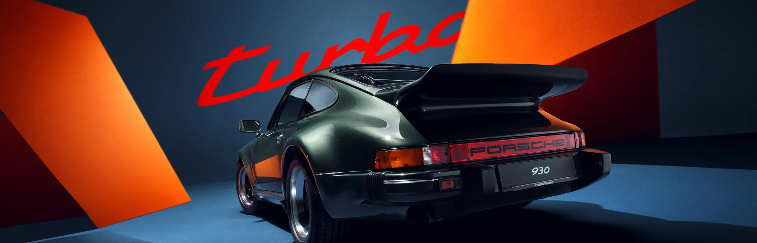 Une Porsche 911 Turbo (930) vue de trois quarts arrière, devant un fond Bleu Orange. 