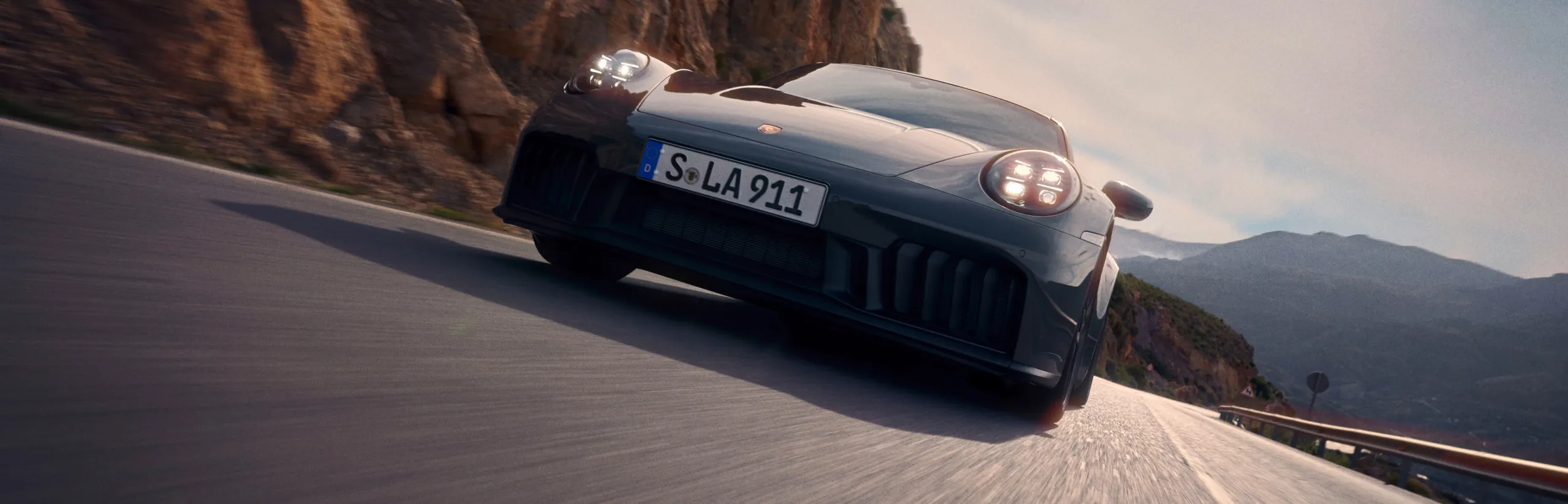 Porsche 911 Carrera GTS in Slate Grey Neo driving on a road. Front view from the front.