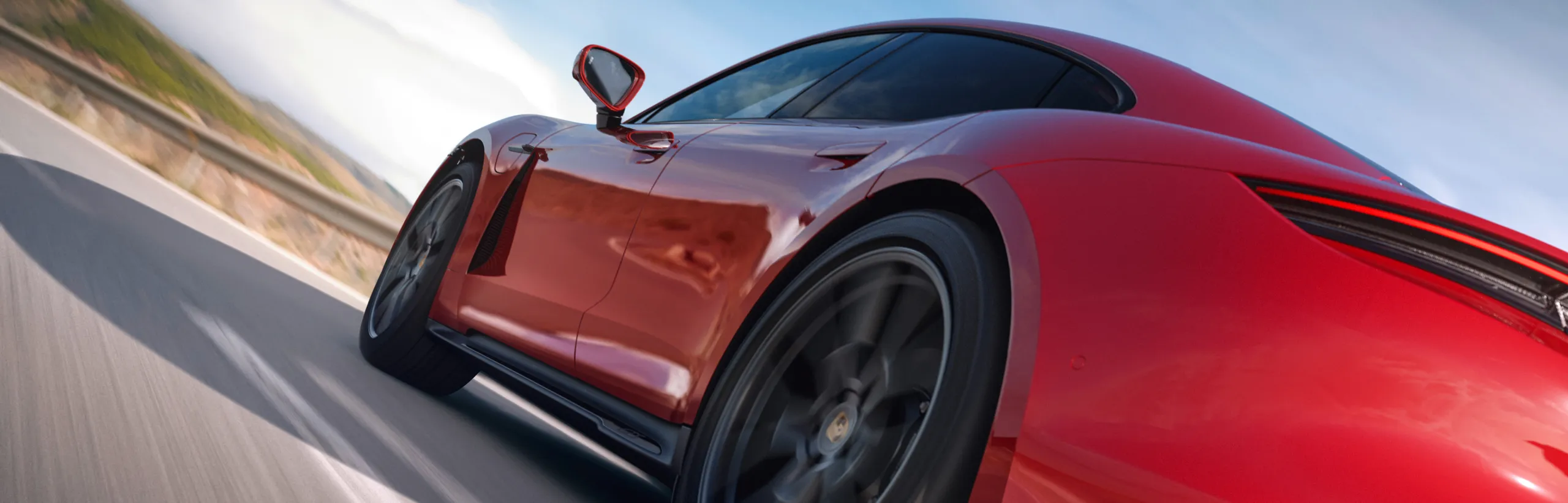 Zicht op de achterkant en zijkant van de rijdende Porsche Taycan GTS in karmijnrood.